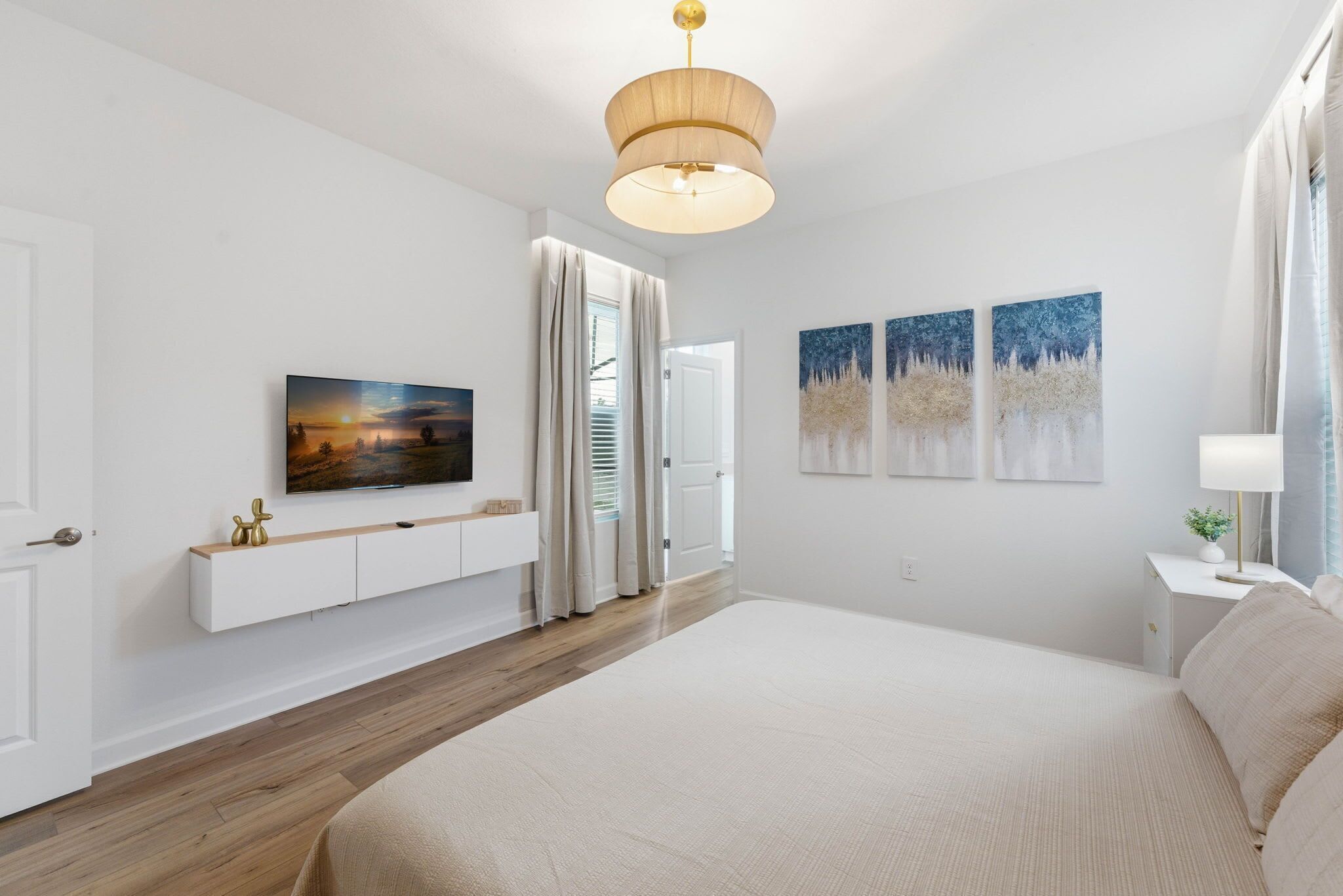 Ein Schlafzimmer mit einem großen Bett, einem Wand-Fernseher, einer Deckenleuchte und Bildern an der Wand.