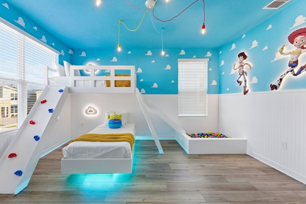 A child's bedroom with a bunk bed, a slide, and a wall with cloud decals.