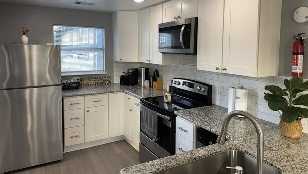 A modern kitchen with white cabinets, stainless steel appliances, a microwave, a coffee maker, and a sink. - Amazing 2-bedroom house in beautiful Houston with AC (Houston)
