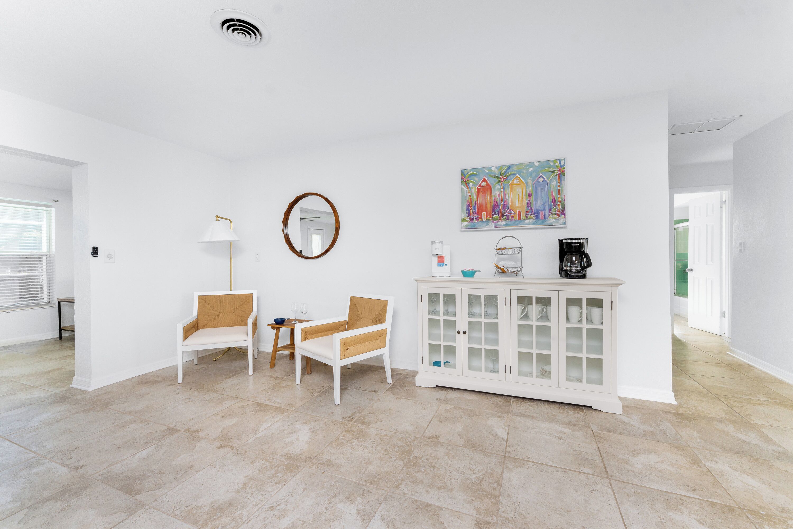 A spacious living area with a white cabinet, two chairs, a small table, and a painting on the wall.