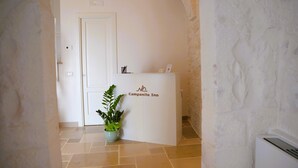 Una recepción con el letrero de Campanile Inn, una planta en maceta y una puerta en un pasillo con paredes de piedra y piso de baldosas.