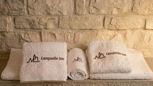 Tres toallas dobladas cuidadosamente, con el bordado 'Campanile Inn', apoyadas contra una pared de piedra texturizada.