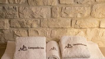 Tre asciugamani piegati con cura, con ricamato 'Campanile Inn', appoggiati su una parete in pietra strutturata.