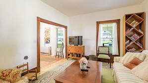 A living room with a sofa, a coffee table with flowers, a TV, a bookshelf, and a door leading to a balcony. - Amazing 2-bdrm apartment in quintessential coastal Friendship, Maine - 1st floor (Friendship)