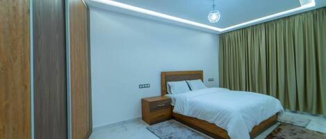 A bedroom with a bed, nightstands, a wooden wardrobe, and a ceiling light fixture.