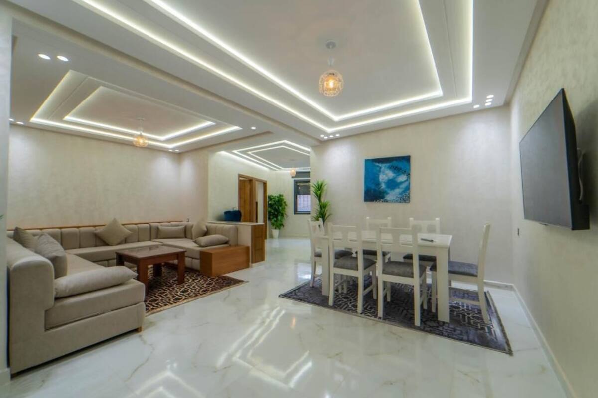 Una sala moderna con un sofá modular, una mesa de comedor con sillas y un televisor de pantalla plana montado en la pared.