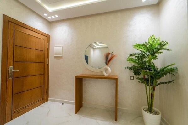 A hallway with a wooden door, a round mirror on a wooden console, and a potted plant. - Dar bensaid (Chefchaouen)
