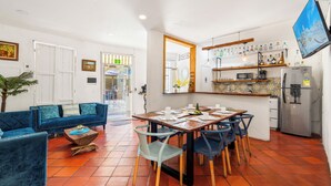 Ein modernes Wohnzimmer mit einem blauen Sofa, einem Esstisch mit Stühlen und einer Küchenzeile inklusive Kühlschrank und Regalen.