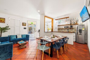 A modern living room with a blue sofa, a dining table with chairs, and a kitchen area with a refrigerator and shelves. - Casa Trinidad - Luxury 9BR House in the Old City w/ Cook & Security (Cartagena de Indias)