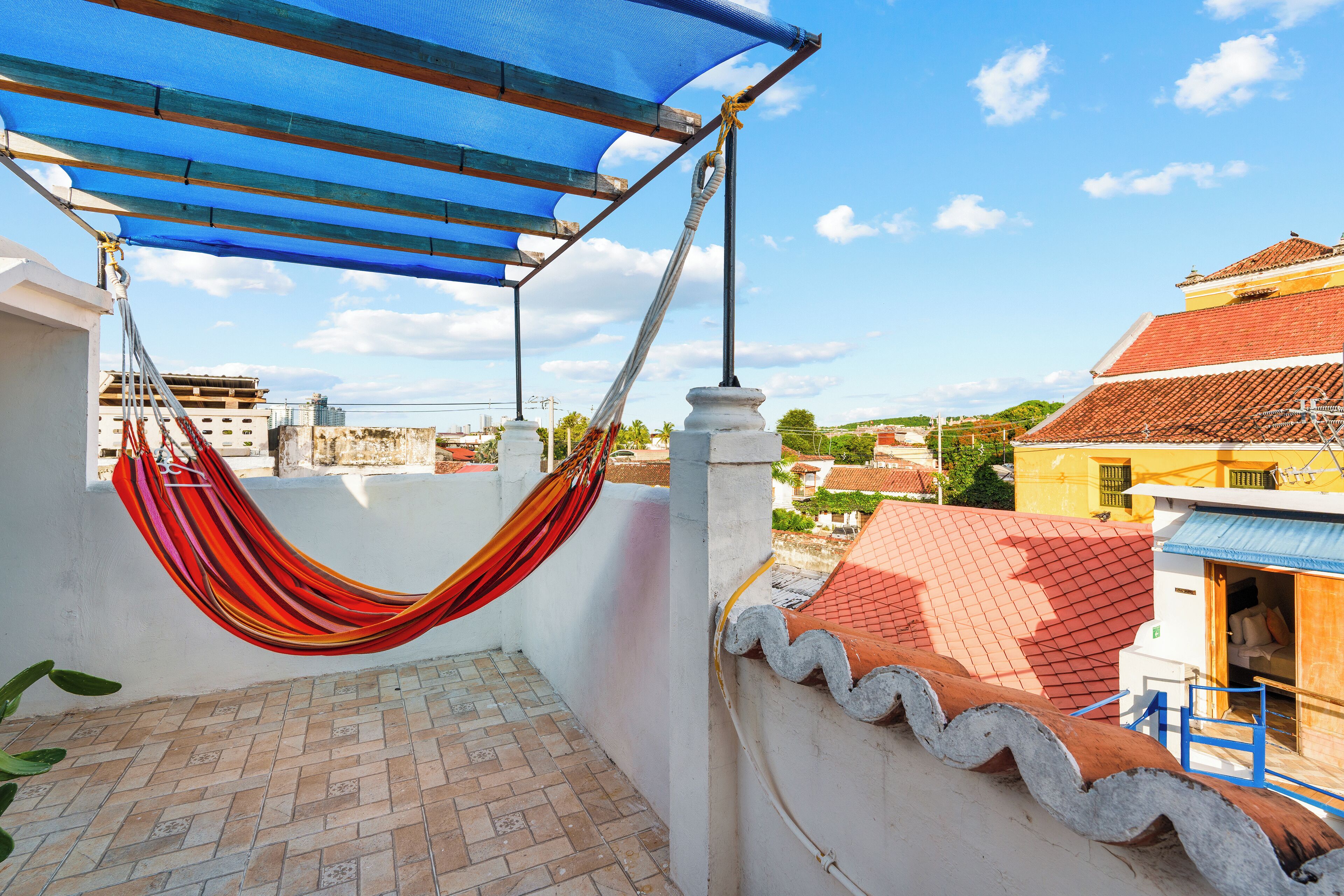 A rooftop terrace with a hammock, a blue shade, and a view of the cityscape.