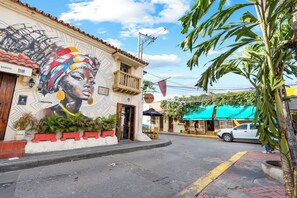 A street with a mural, a white car, and a building with a balcony. - Casa Trinidad - Luxury 9BR House in the Old City w/ Cook & Security (Cartagena de Indias)