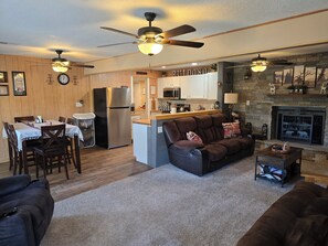 A cozy living room with a fireplace, a dining area with a table and chairs, and a kitchen with wooden cabinets and a refrigerator. - 2 BD/2 BA - 5 min to Midtown - Close to Ski Apache (Ruidoso)