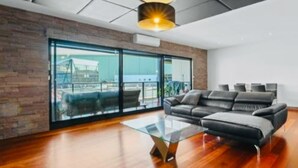 A modern living room with a sectional sofa, a glass coffee table, and a large sliding glass door leading to an outdoor area. - Waterfront Marina Escape (Patterson Lakes)