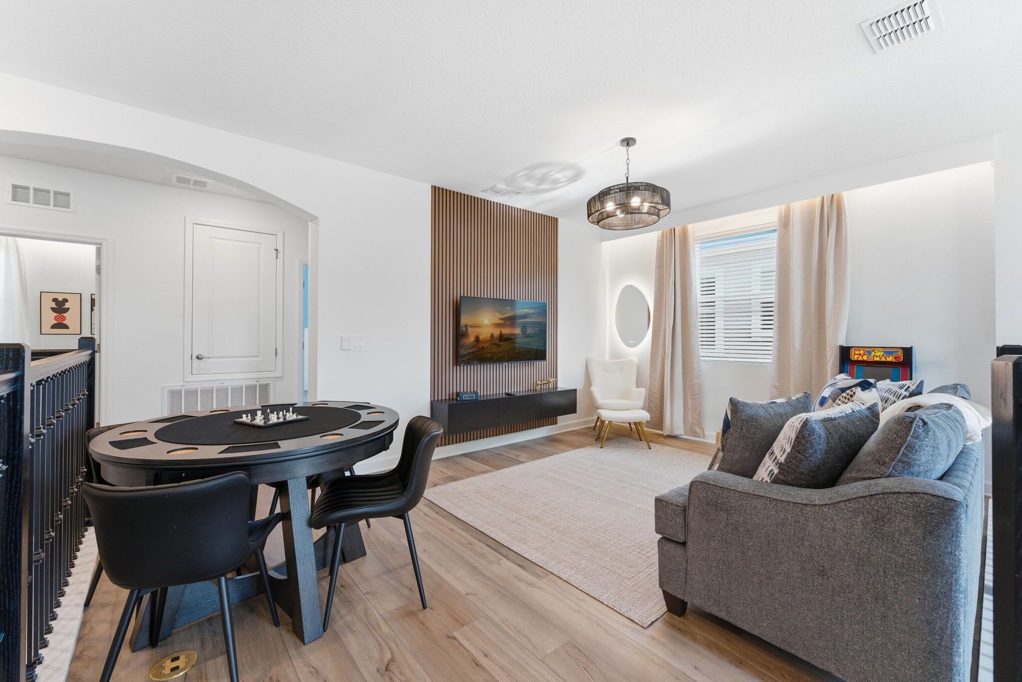 A modern living room with a round dining table, black chairs, a grey sofa, and a large painting on the wall.