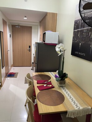 A dining area with a wooden table, red napkins, and a cityscape poster on the wall. - Cozy 1-bedroom condo in serene Pasay City with AC (Pasay City)