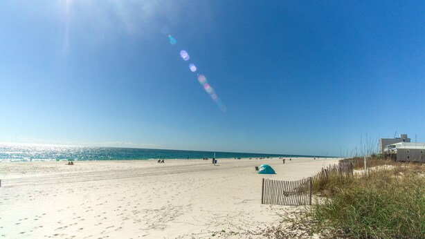 Ein Strand mit sandigem Ufer, einigen Personen und einem Gebäude im Hintergrund.