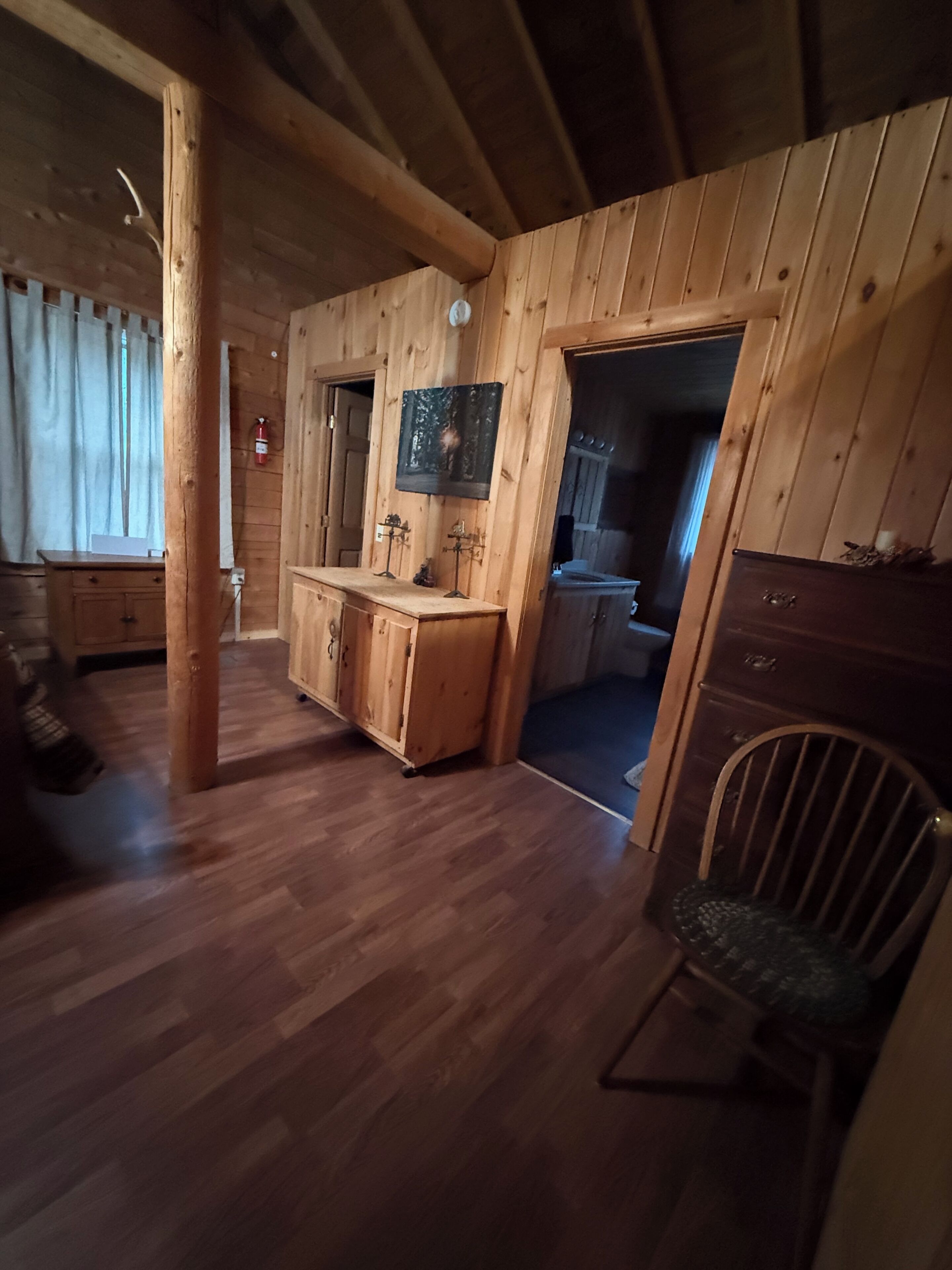 A wooden interior with a wooden bench, a wooden cabinet, and a door leading to another room.