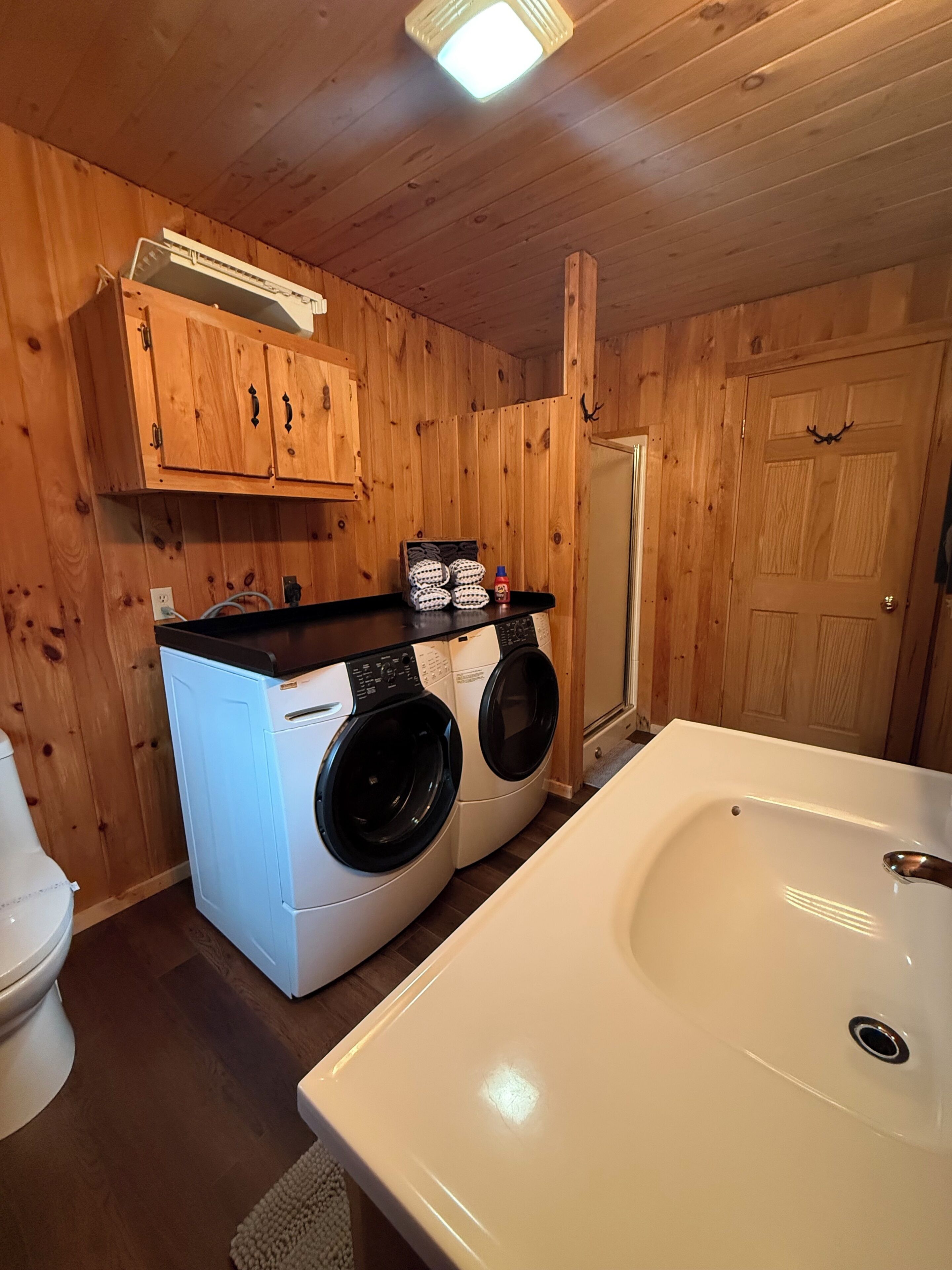 A laundry room with two front-loading washers, a white sink, wooden walls, and a door.