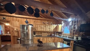 A wooden kitchen with a central island, stainless steel appliances, and hanging pots. - Cozy 3-bedroom rustic lodge in Island Falls perfect for your getaway (Island Falls)