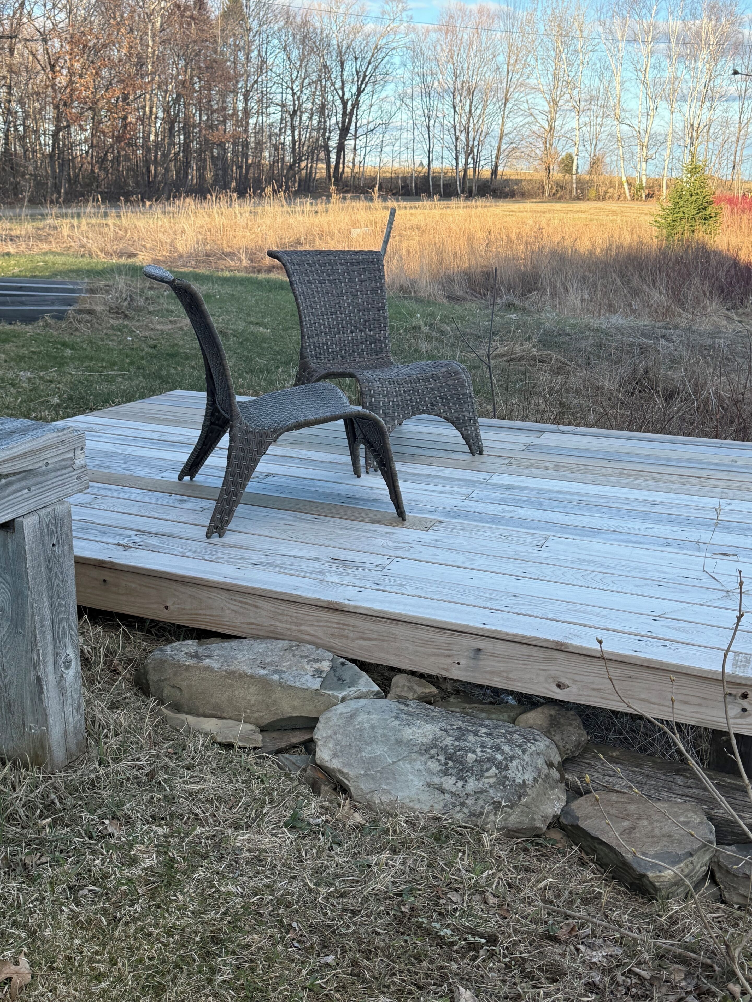 Eine Holzterrasse mit zwei Korbstühlen und einer Steinbank.