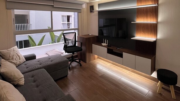 Ein modernes Wohnzimmer mit einem grauen Sofa, einem schwarzen Bürostuhl, einem Fernseher und Holzboden.