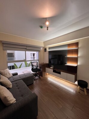 A modern living room with a grey sofa, a black office chair, a TV, and a wooden floor. - Modern Apartment in Lima - Chorrillos   (Chorrillos)