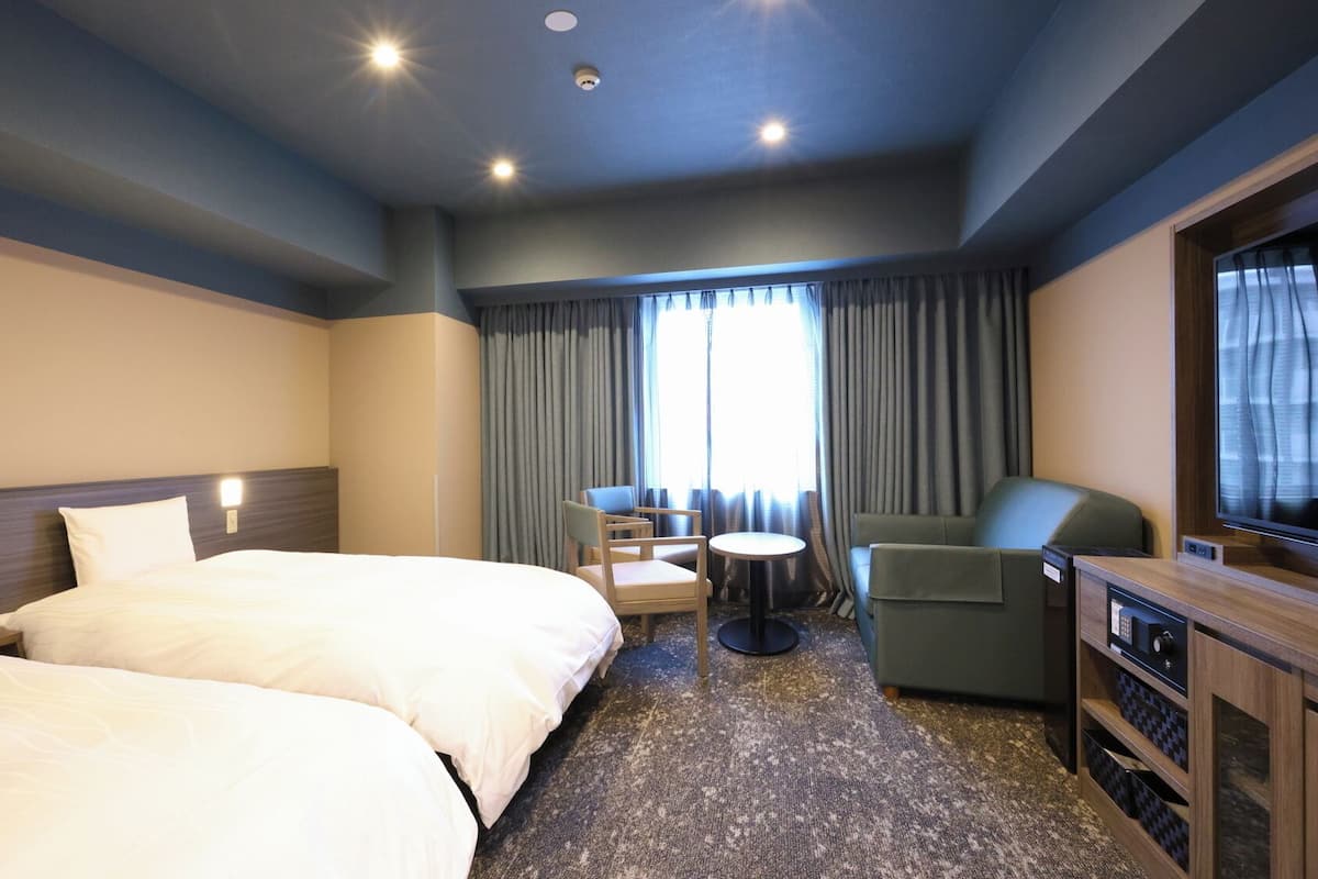 Ein Hotelzimmer mit zwei Betten, einem Schreibtisch, einem Stuhl, einem Fernseher und einem Fenster mit Vorhängen.