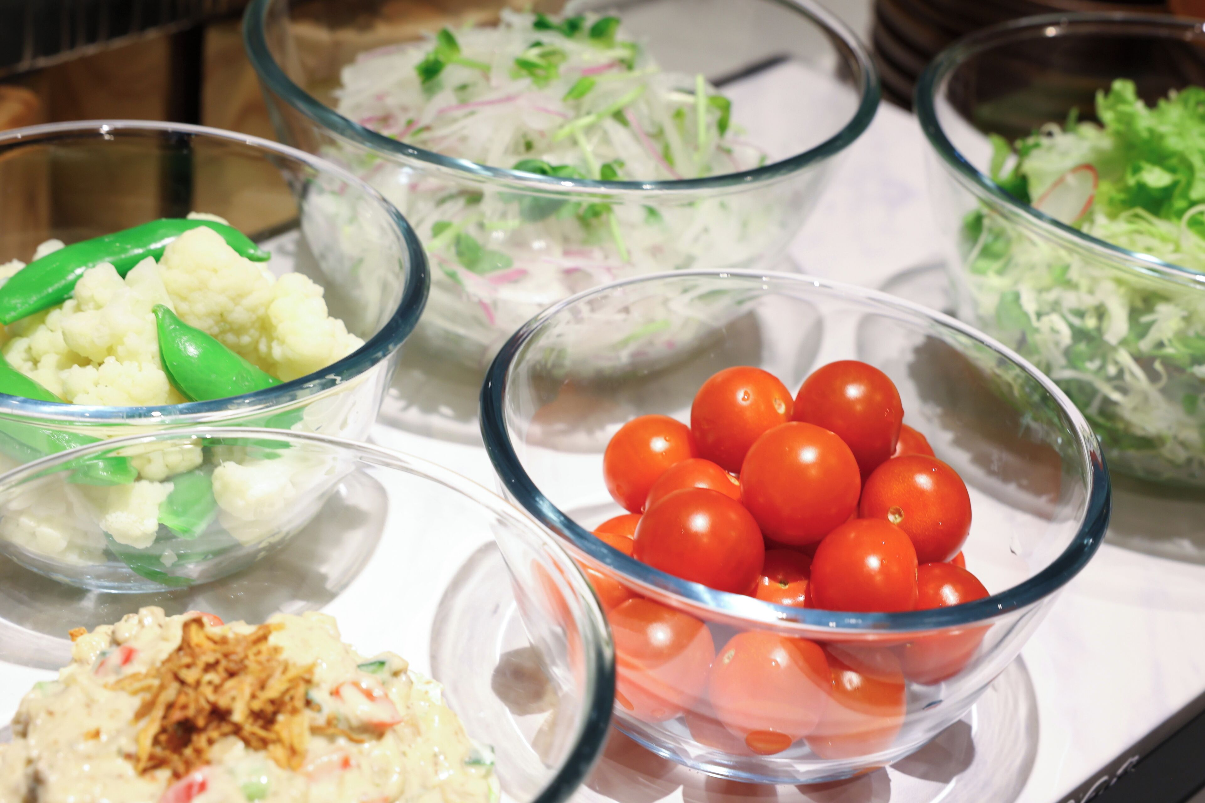 A buffet table with various food items including a bowl of cherry tomatoes, a bowl of cauliflower, and a bowl of salad.