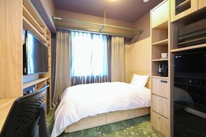 Ein Hotelzimmer mit einem Bett, einem Schreibtisch, einem Stuhl, einem Fernseher, einem Kleiderschrank und einem Fenster mit Vorhängen.
