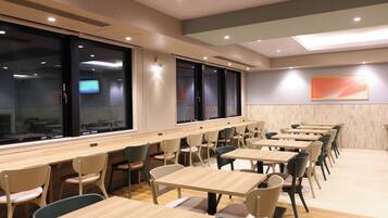 Un comedor moderno con varias mesas y sillas, ventanas amplias y un televisor montado en la pared.