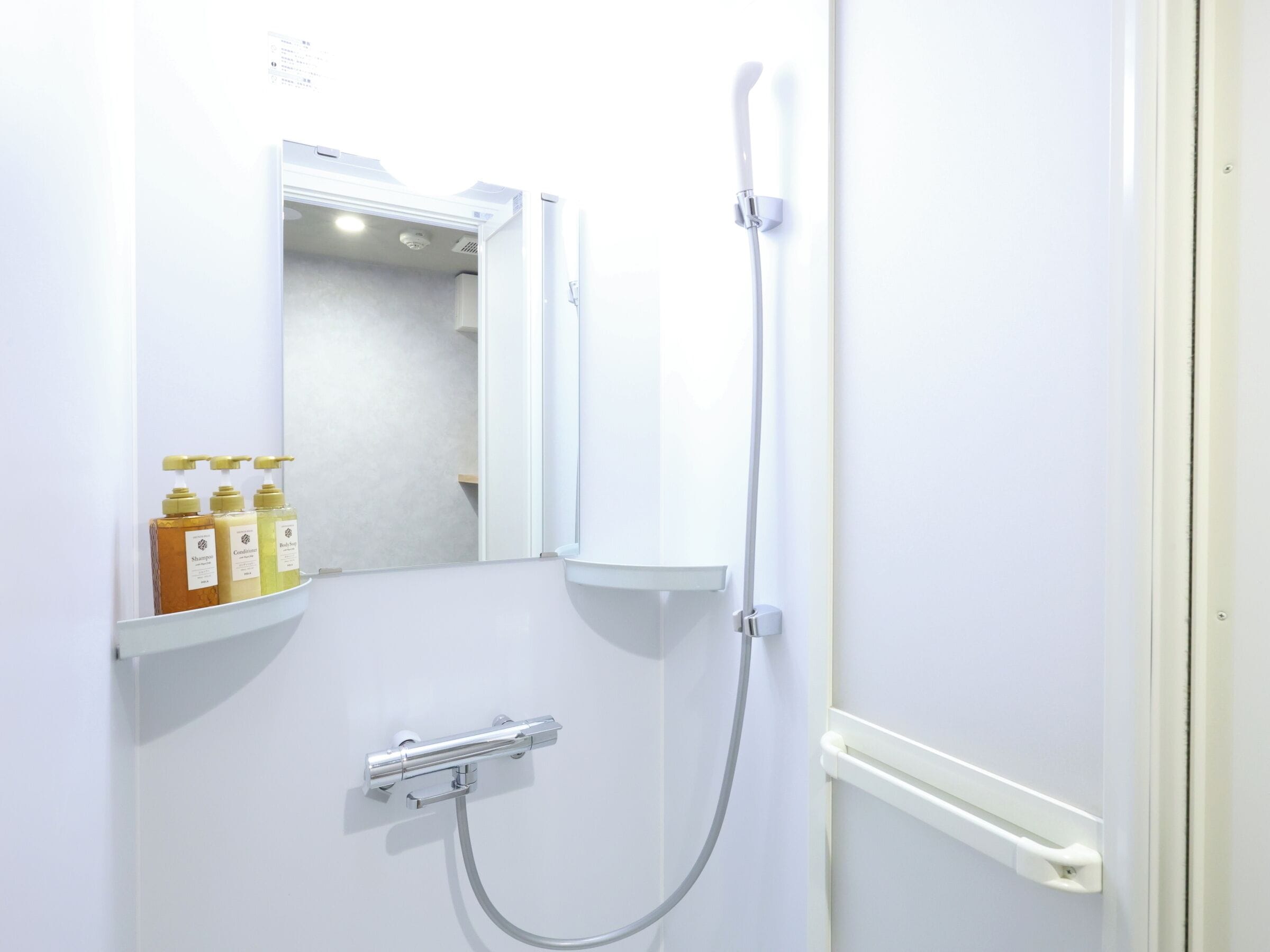 A bathroom with a shower, a mirror, and a shelf with toiletries.