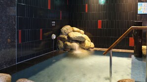 A hot spring area with a stone waterfall, tiled walls, and a wooden railing. - Natural Hot Springs Higoromo no Yu Dormy Inn Yokkaichi (Yokkaichi)