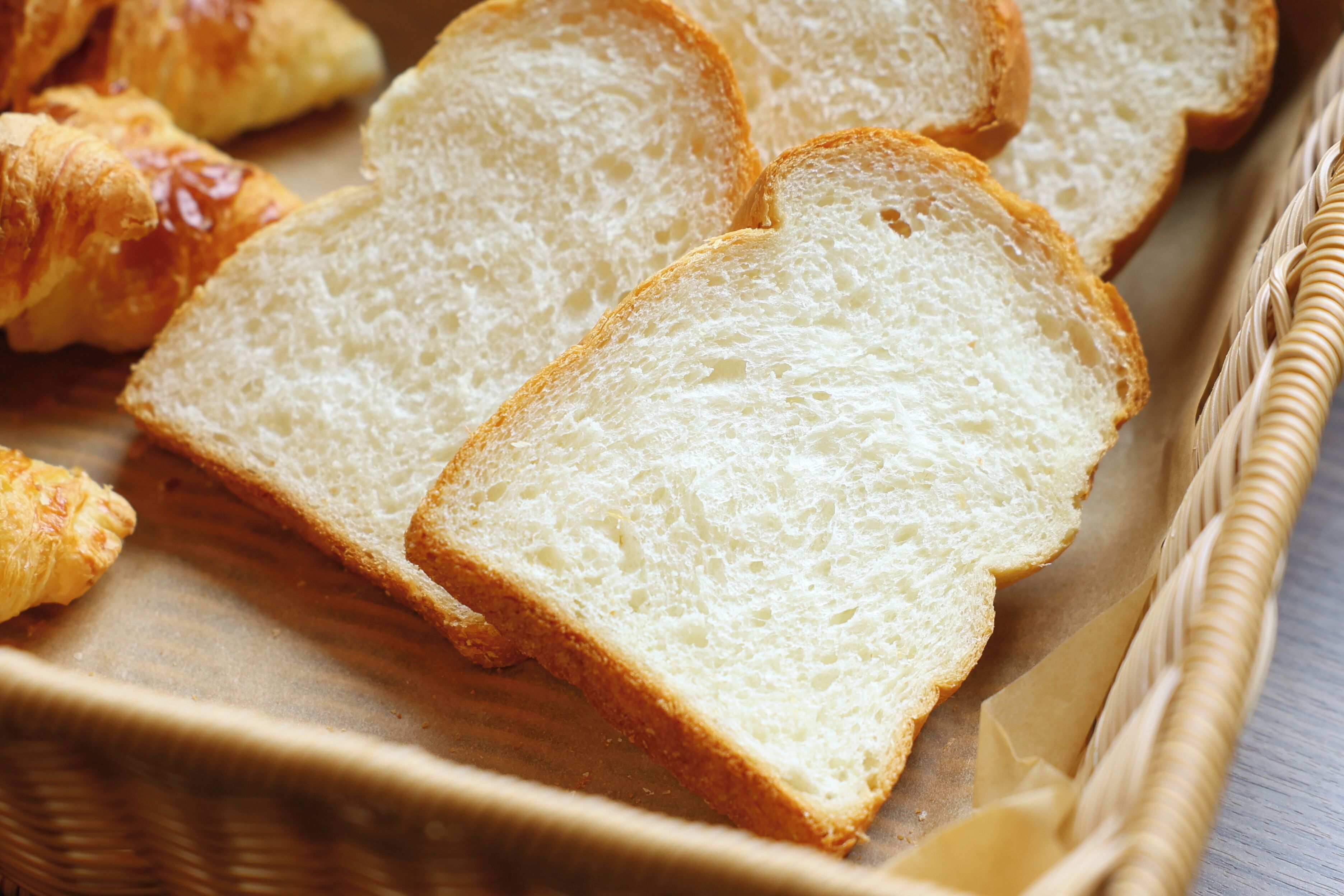 Slices of white bread and croissants in a wicker basket.