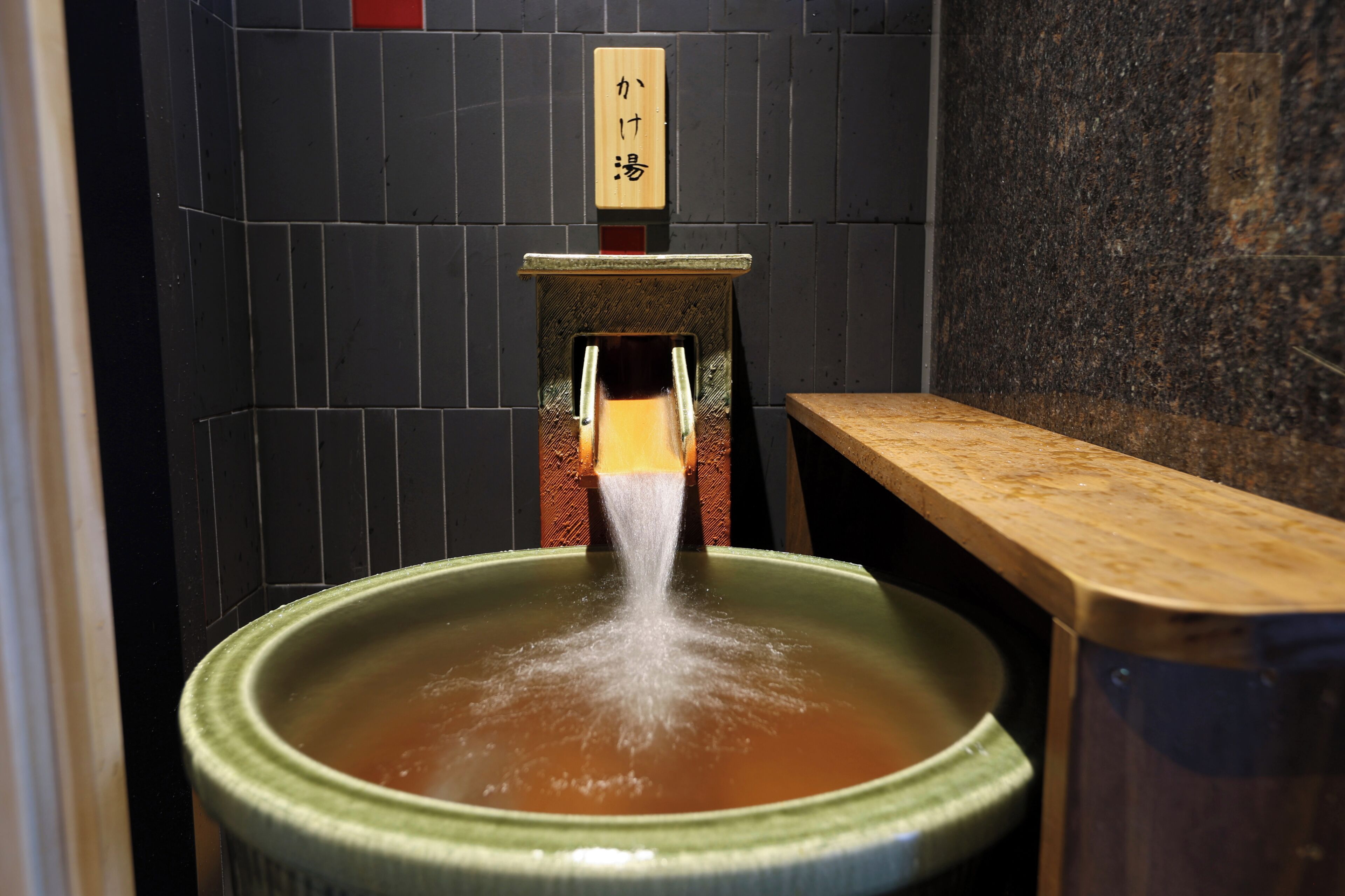 A traditional Japanese onsen with a wooden sign, a stone wall, and a wooden bench.