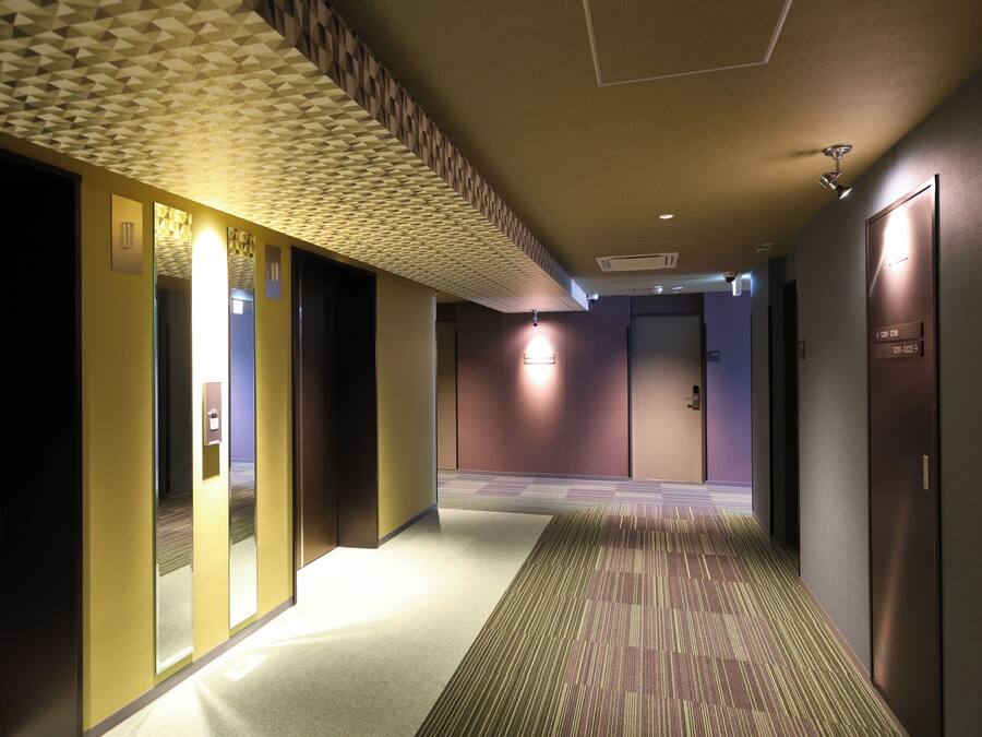 Corredor de hotel com carpete estampado, iluminação embutida e design geométrico no teto.