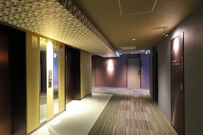 Un pasillo de hotel con alfombra estampada, iluminación empotrada y un diseño geométrico en el techo.