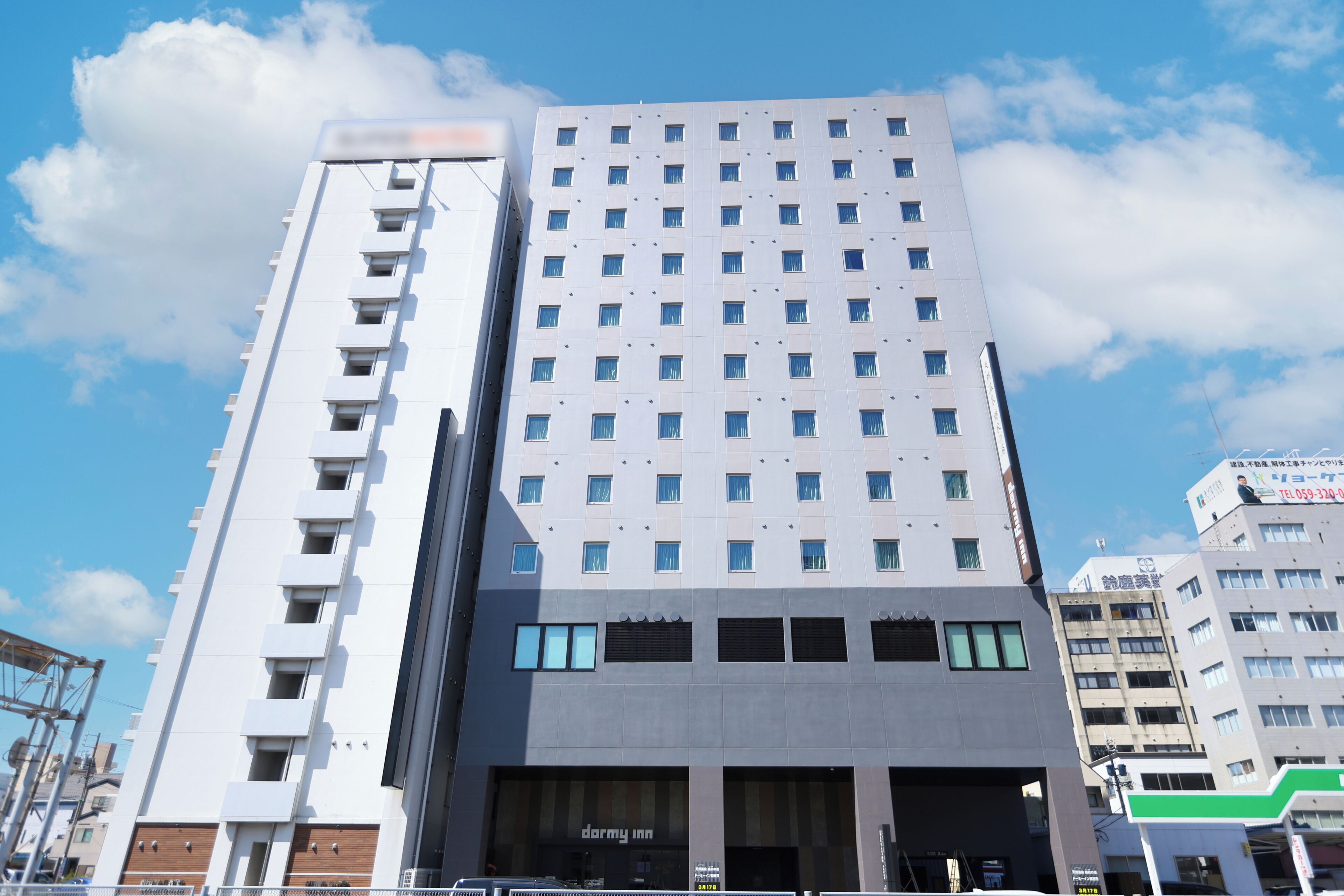 Un hotel de varios pisos con un diseño moderno, que presenta un llamativo letrero de 'dormy inn' a nivel de calle.