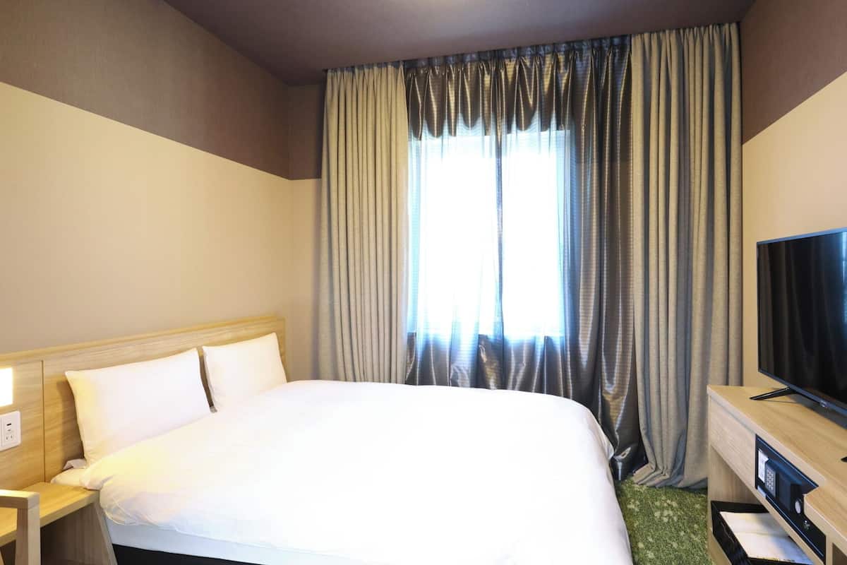 Ein Hotelzimmer mit einem großen Bett, einem Flachbildfernseher, einem Nachttisch und einem Fenster mit Vorhängen.