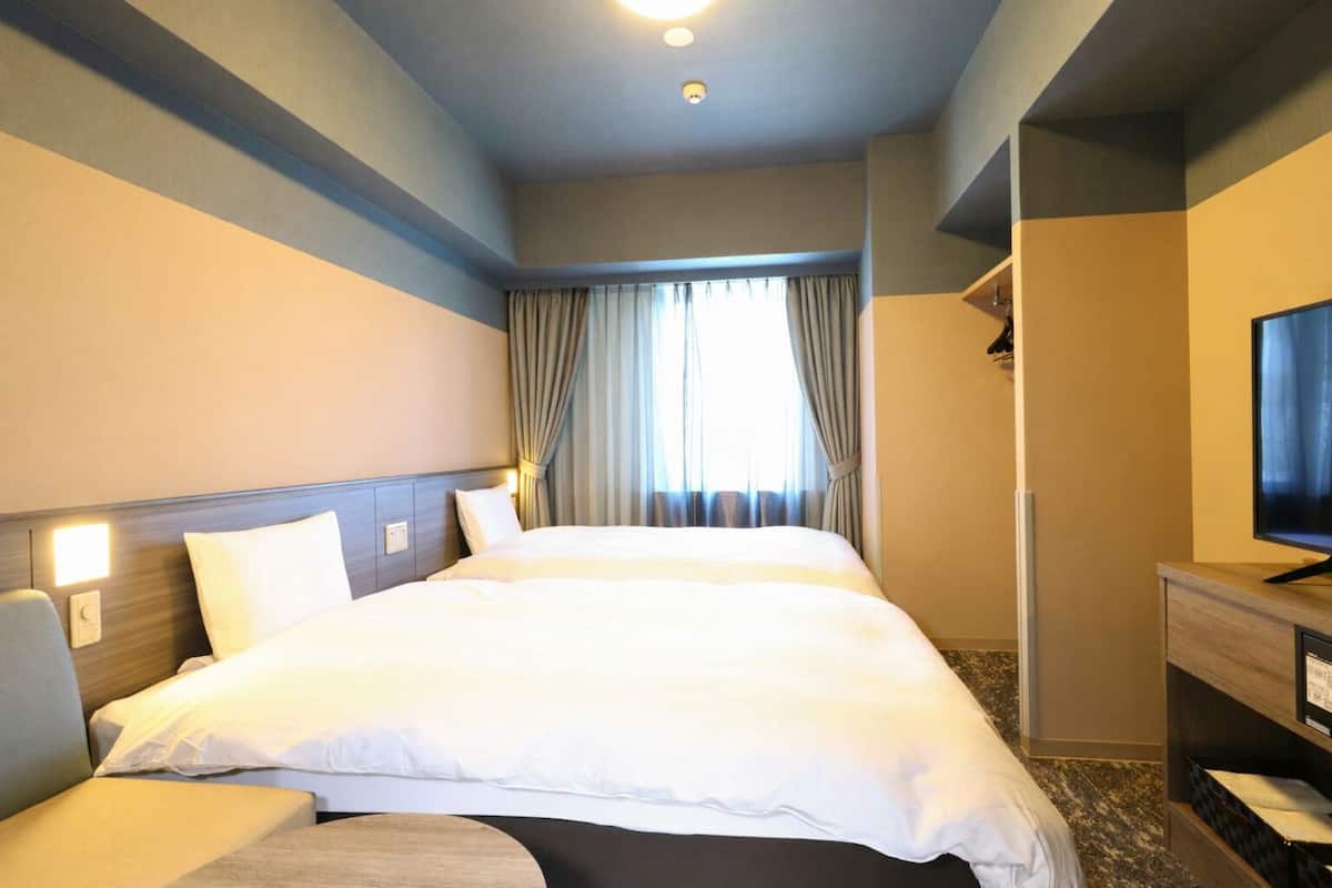 Ein Hotelzimmer mit einem großen Bett, einem Fernseher, einem Schreibtisch und einem Fenster mit Vorhängen.