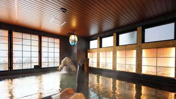 A traditional Japanese onsen with a wooden interior, a stone hot spring, and a view of the landscape through the windows. - Natural Hot Springs Higoromo no Yu Dormy Inn Yokkaichi (Yokkaichi)