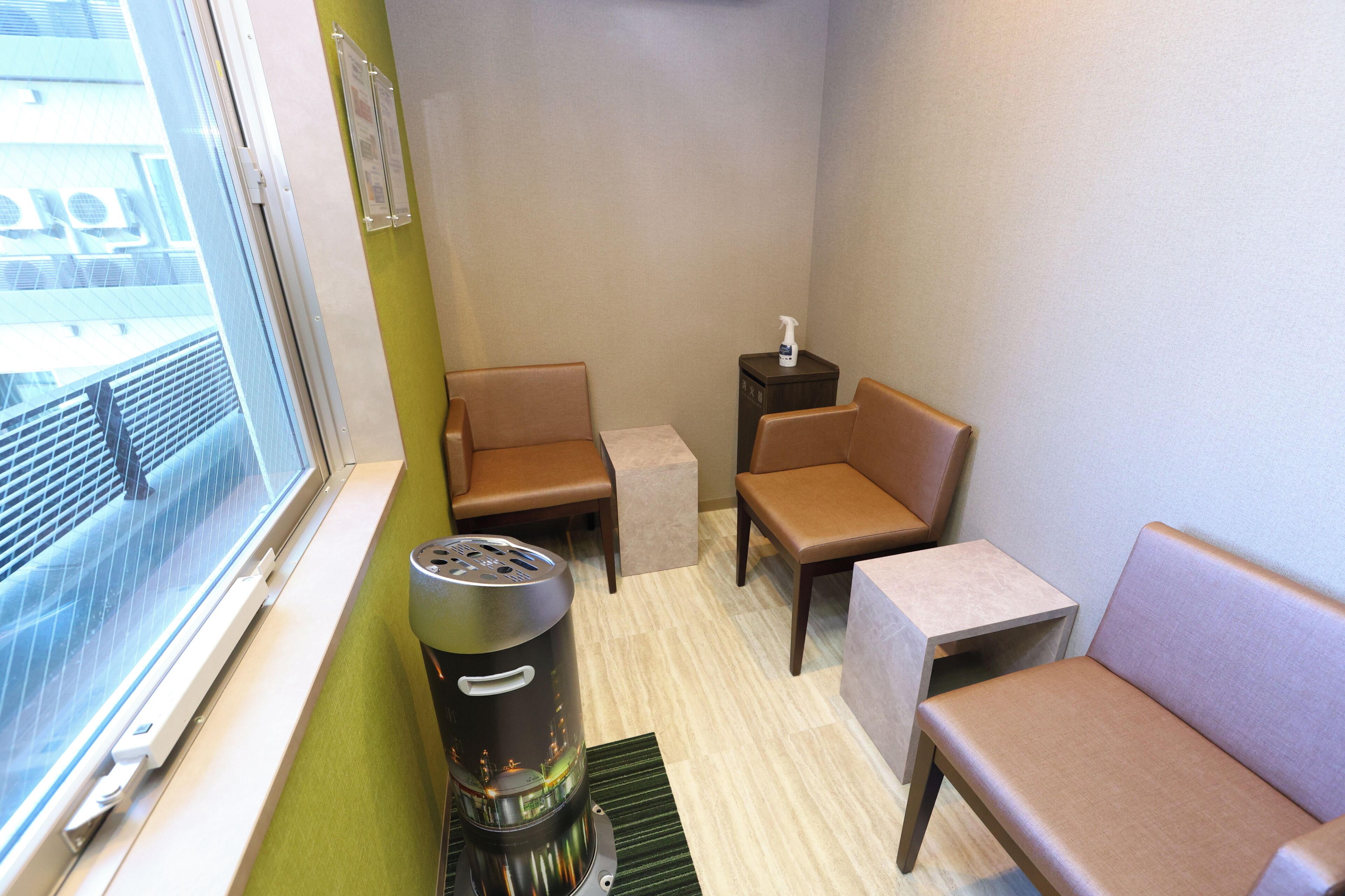 Een kleine, compacte kamer met een raam, een verwarming, twee stoelen, een kleintje tafeltje en een wandplank.