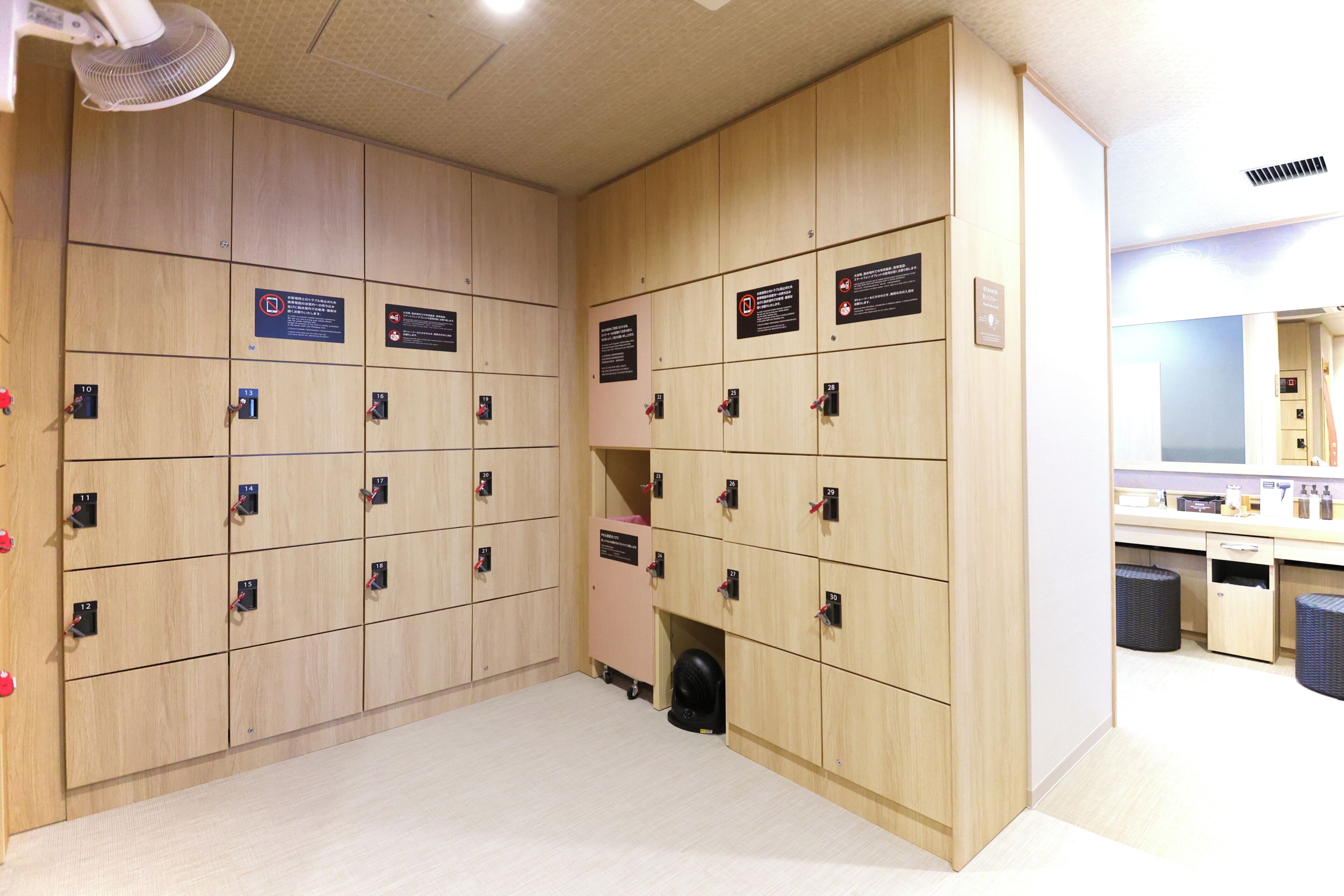 A row of wooden lockers with numbered tags, a fan, and a mirror in the background.