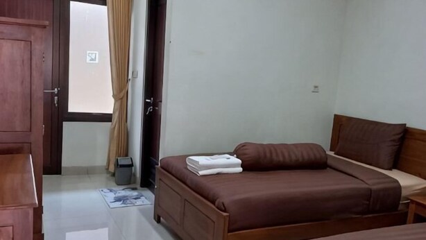 A bedroom with two beds, a wooden wardrobe, and a door leading outside. - Omah Paulan Guest House (Colomadu)
