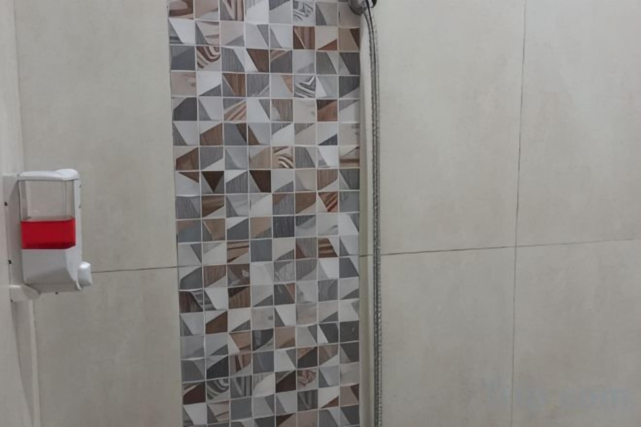 A shower area with a tiled wall, a hand soap dispenser, and a showerhead.