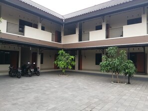 A courtyard with tiled flooring, two potted plants, and a row of parked motorcycles. - Omah Paulan Guest House (Colomadu)