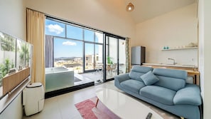 Un salon moderne avec un canapé, un téléviseur et une vue sur le paysage urbain, grâce à de grandes fenêtres.