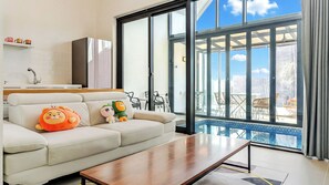 Una sala de estar moderna con sofá, mesa de centro y juguetes de peluche. Un ventanal ofrece vistas del exterior.
