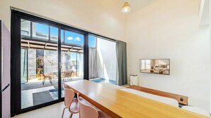 Un comedor moderno con una mesa de madera y sillas rosa, grandes puertas correderas de vidrio que dan a un patio exterior, y un cuadro en la pared.