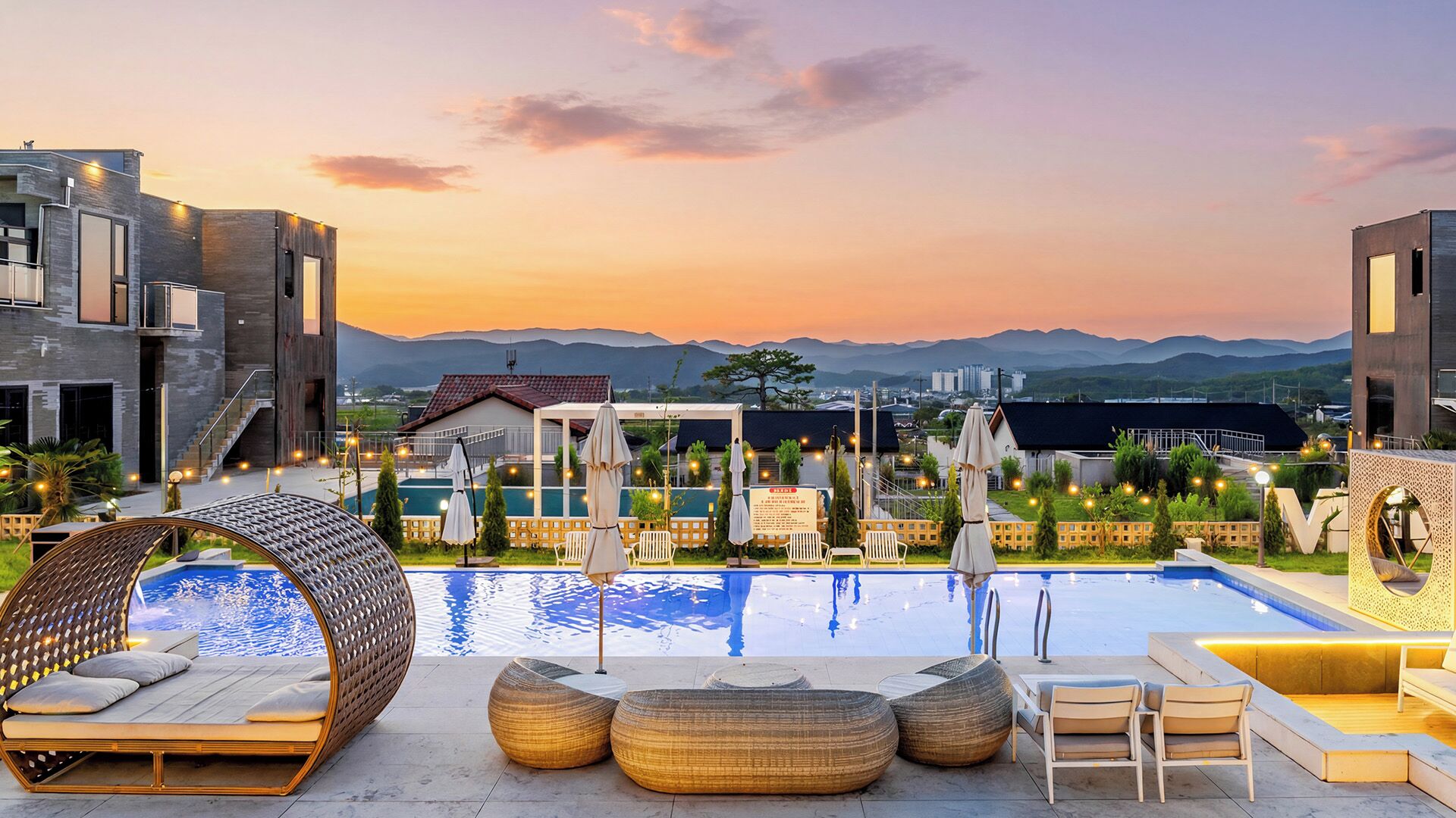 Un espace piscine avec des chaises longues et une vue sur les montagnes au coucher du soleil.
