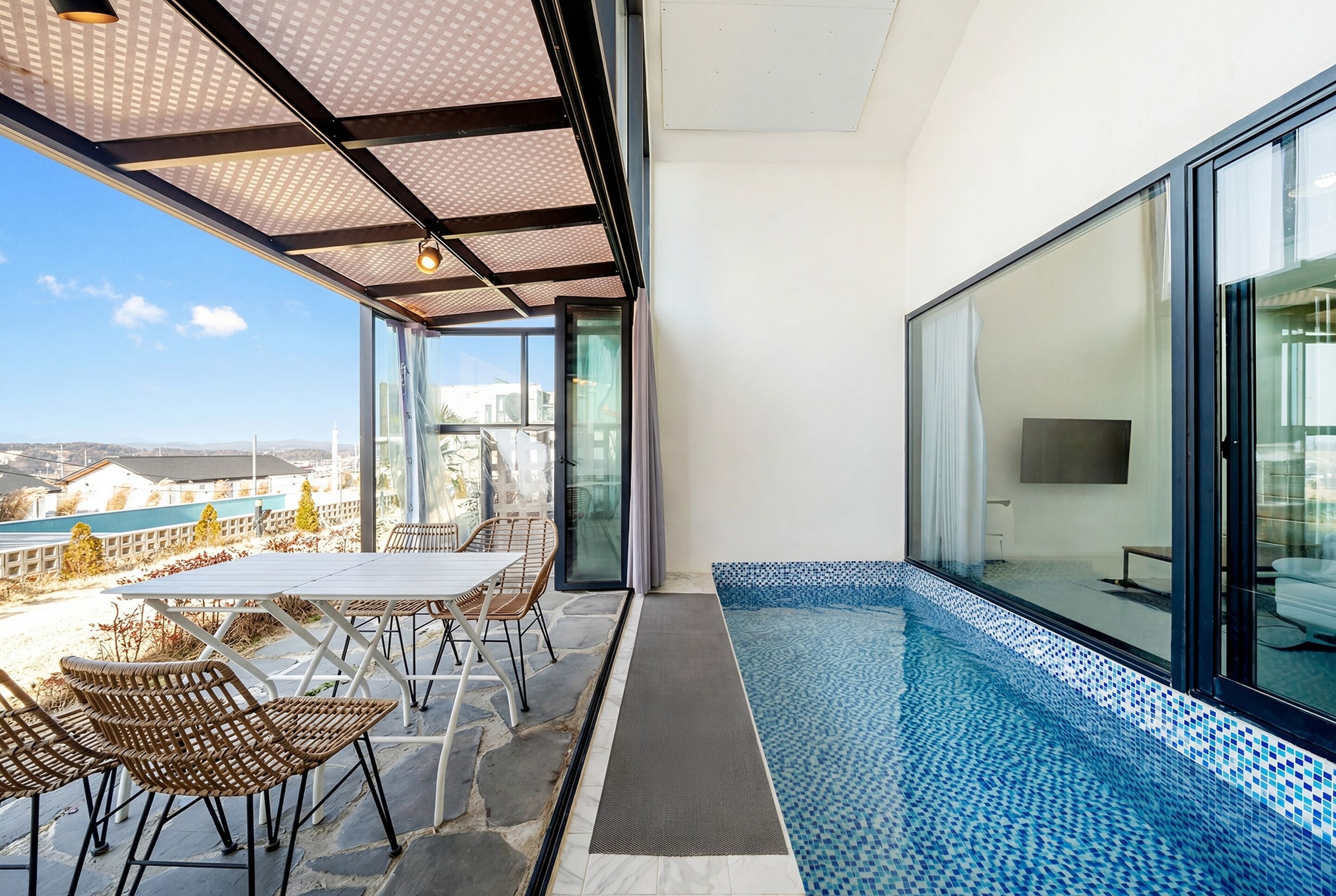 A balcony with a glass door leading to a pool area, a table with chairs, and a view of the cityscape.